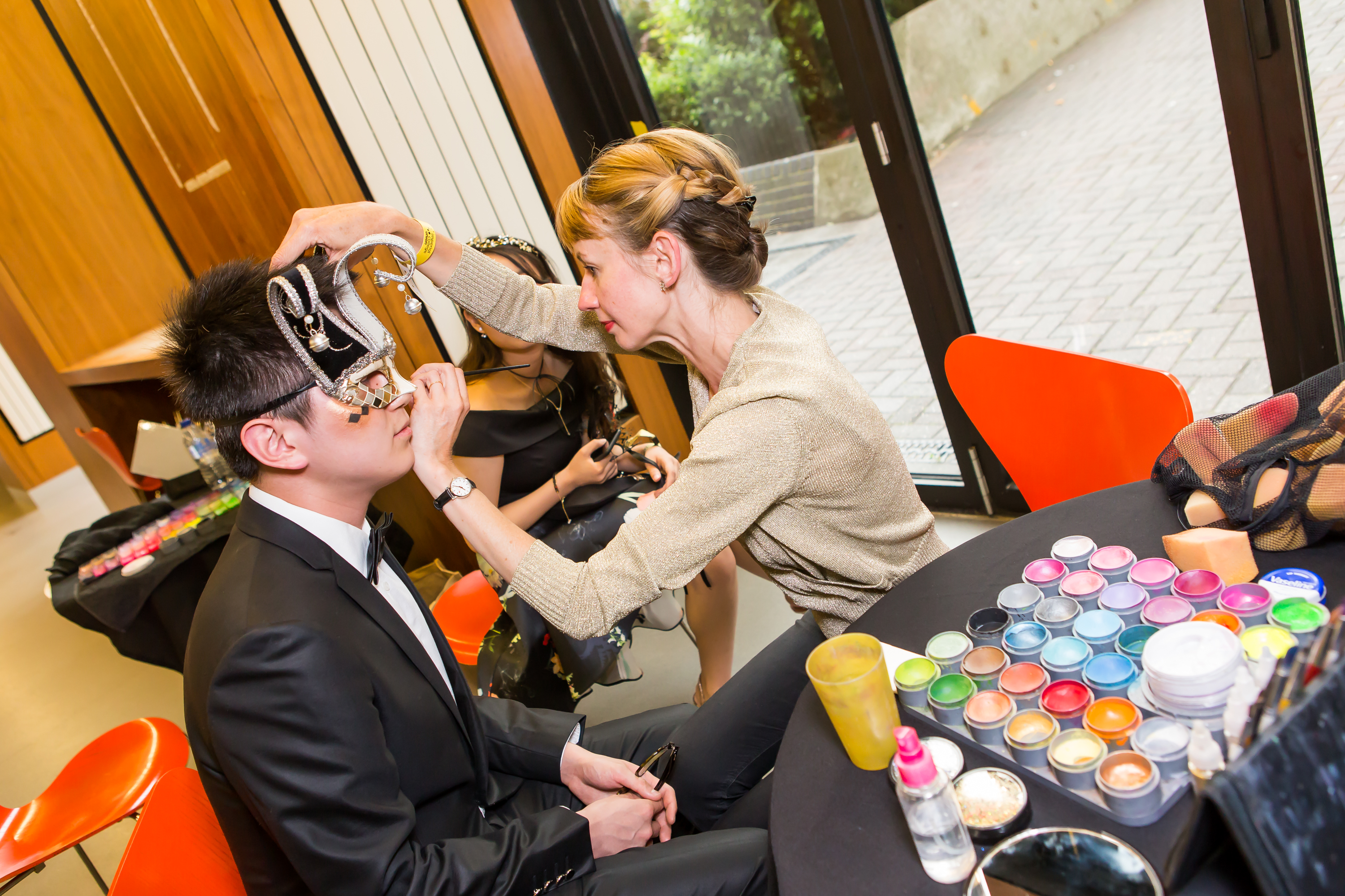 Make-up artist painting student's face, side-on view.