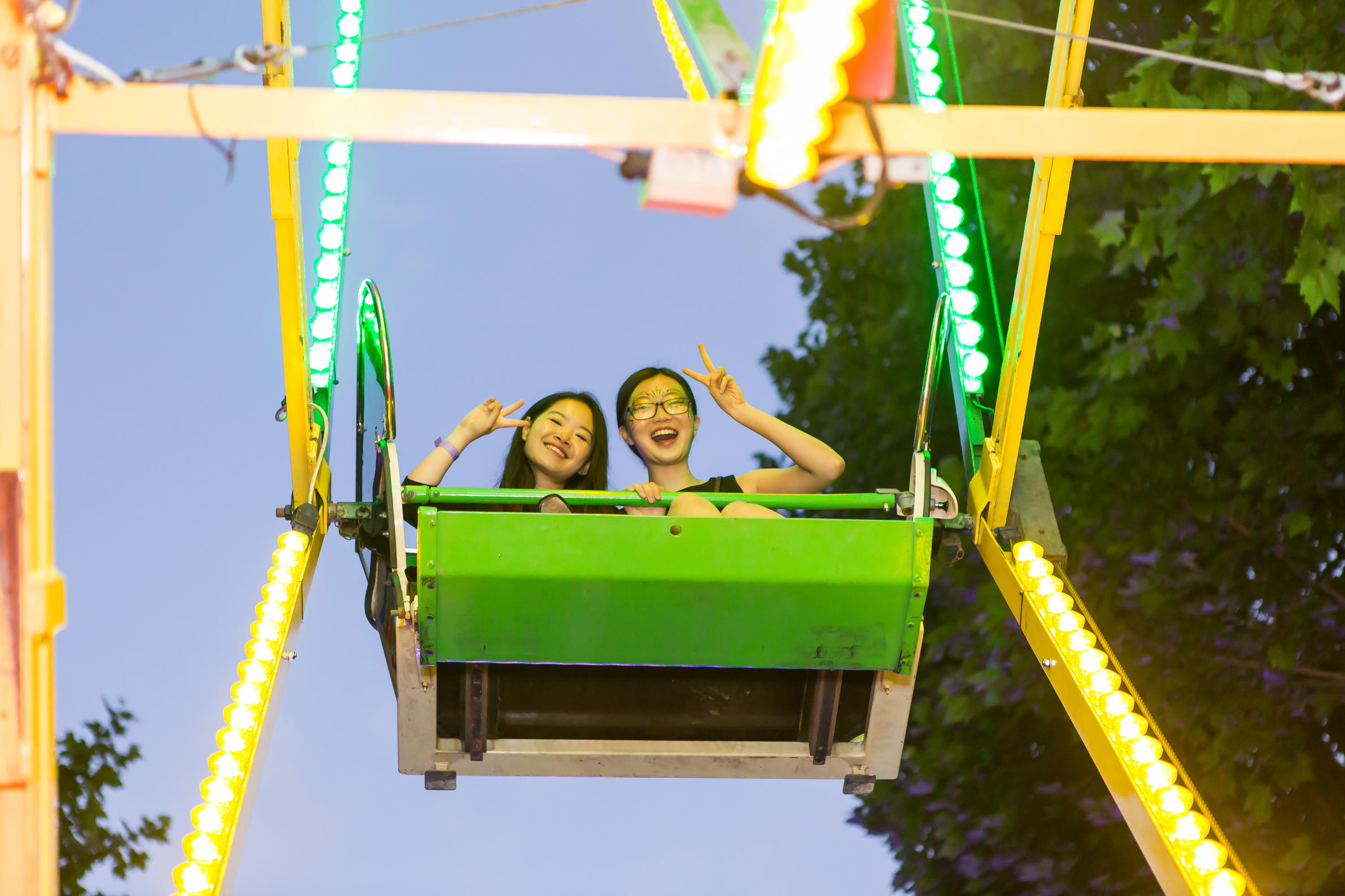 Two students looking down and waving from their seat on the big wheel.