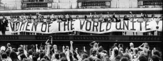 Black and white, vintage photo depicting a crowd of women holding a big banner with text: Women of the world unite!