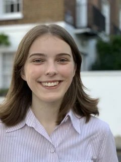 Anthea has mid length brown hair and is smiling. She is wearing a white collared shirt.